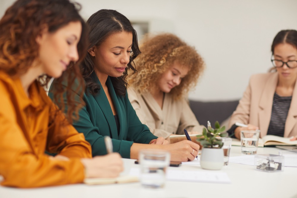 Group of four successful multi-ethnic businesswomen working in team sitting together in modern office room